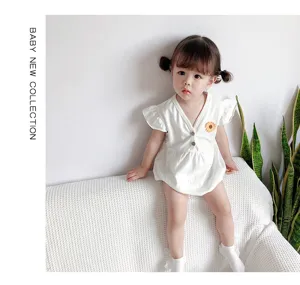 Detalle del body de bebe de algodon blanco con bonita flor pequena sobre sofa blanco.