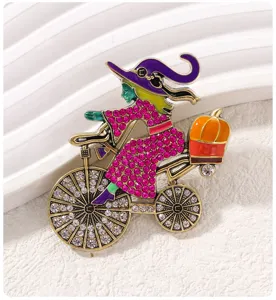Halloween witch riding bicycle brooch with rhinestones and pumpkin accent for women fashion.