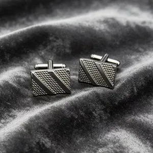 Close-up shot of men's dark metal rectangular cufflinks featuring textured diagonal stripe details.