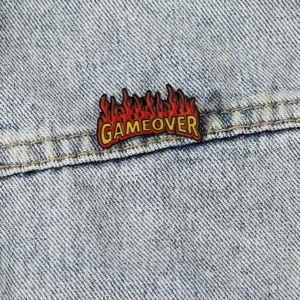 Broche de esmalte con letras GAMEOVER estilo punk y diseño de llama vista detallada.