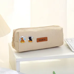 Beige canvas pencil case with cute cartoon patches and basic leather label, stylish stationery bag.