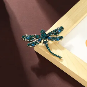 Detail shot of a vintage style dragonfly brooch with green and blue rhinestones on a wooden frame.