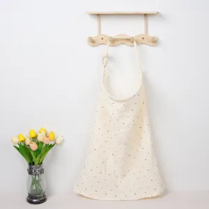 Close-up detail of cotton nursing cover with colorful dots hung on wooden wall rack.