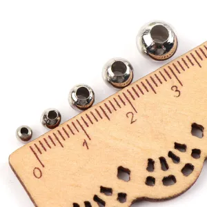 Close-up view of electroplated metal beads in various sizes on a wooden ruler for DIY crafts.