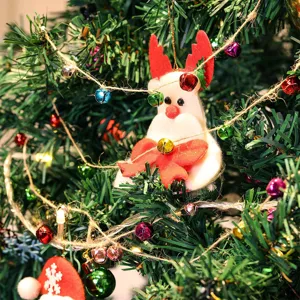 Gros plan sur les détails du sapin avec des cloches métalliques et un ornement en feutre.