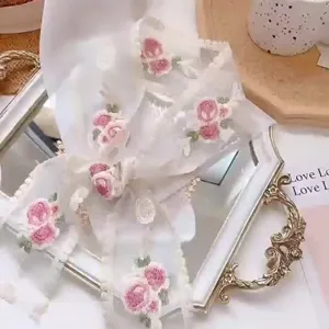White lace ribbon detail featuring delicate pink rose embroidery for elegant gift packaging.