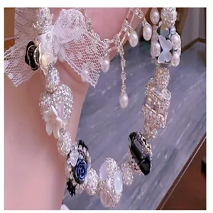 Handgefertigtes DIY Perlenaccessoire Detail mit Strass, Perlen, Spitze und Blumenanhängern.