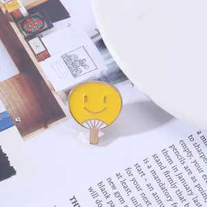 Detail shot of a cute yellow fan-shaped smiley face enamel pin, stylish alloy clothing badge.