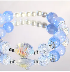 Close-up detail of blue crackle glass bead bracelet with iridescent shell charm and spacer beads.