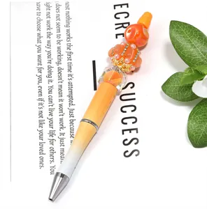 Détail de gros plan d'un stylo à bille DIY perlé avec dégradé orange et couronne de strass.