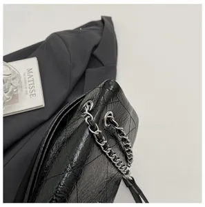 Detailaufnahme der schwarzen gesteppten Kettenschultertasche aus glänzendem Leder.