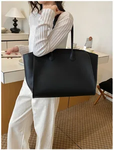 Black leather commuter tote bag displayed in a clean indoor setting, large capacity design.