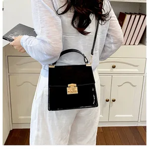 Detailaufnahme einer schwarzen Lackleder Handtasche mit goldenem Schloss und Riemen, Lifestyle.
