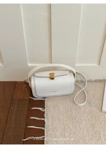 Dettaglio della borsa a mano bianca minimalista con chiusura dorata e trama elegante.