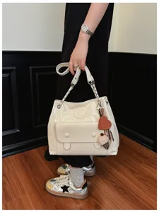 Detailed view of cream white shoulder bag with chain strap and cute heart charm accessory.