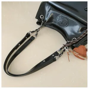 Detailed view of black patent leather shoulder bag with chain strap and chic pendant charm.