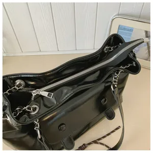 Black patent leather shoulder bag detail, featuring shiny finish, metal chain strap, and zip.