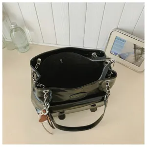 Black patent leather shoulder bag detail showing interior compartment, chain straps and front pocket.