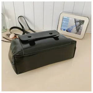 Classic black patent leather shoulder bag detail, vintage flap design with dual buttons.