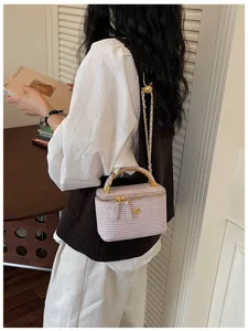 Detailaufnahme einer helllila geflochtenen Kosmetiktasche mit Goldkette und Griff im Raum