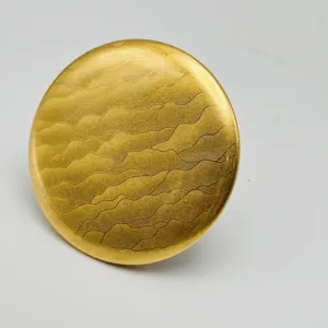 Round gold metal badge backing paper with wavy texture, ideal for custom merch and crafts.