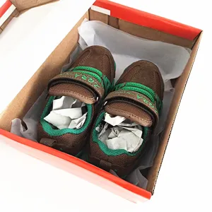 Vista detallada de zapatillas de malla para niños en marrón y verde con tiras de velcro en caja.