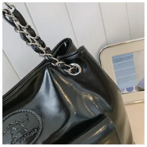 Close-up detail of black patent leather shoulder bag with interwoven chain strap and logo patch.