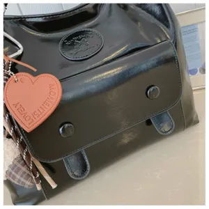 Detailed shot of black patent leather retro shoulder bag with front pocket and heart pendant.