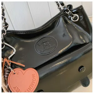 Black patent leather shoulder bag detail with metal chain strap and front pocket design.