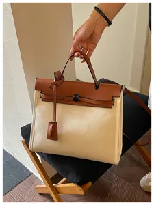 Vue détaillée du sac à main bicolore en toile et cuir avec poignée et bandoulière.