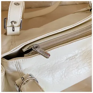 Close-up detail of white pleated hobo bag, stylish commuting tote with metal hardware.