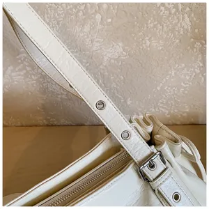 Close-up detail of stylish pleated shoulder bag strap, metal eyelets, and zipper pocket.