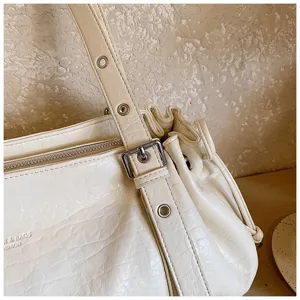 Close-up detail of beige PU leather shoulder bag strap, metal buckle and pleated design.