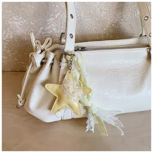 Close-up detail of cream ruched shoulder bag featuring star charm and lace ribbon decor.