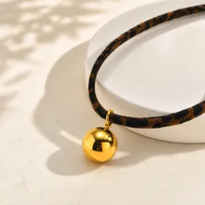 Primer plano de un elegante colgante de bola dorada en un collar de leopardo chic.