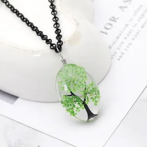 Dettaglio di collana artigianale in resina con ciondolo ovale e albero di fiori secchi.