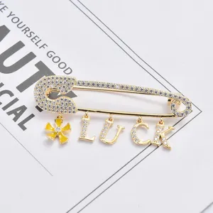 Gros plan sur la broche épingle de sûreté dorée avec zirconiums et pendentifs LUCK.