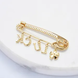 Broche épingle de sûreté dorée avec pendentifs lettres et cristaux, bijou tendance élégant.