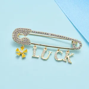 Broche épingle de sûreté dorée avec breloques lettres LUCK et fleur jaune, détail exquis.