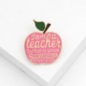Close-up of a cute apple-shaped enamel brooch for teachers with inspiring lettering detail.