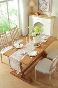 Detail shot of white lace table runner with floral pattern and tassels on wooden dining table.