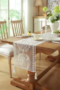 Detail shot of white lace table runner with floral embroidery and elegant tassels for dining room.