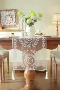 Detailed view of white lace embroidered table runner with delicate floral patterns and tassels.