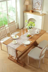 Detail view of white lace table runner with floral geometric embroidery and hanging tassels.