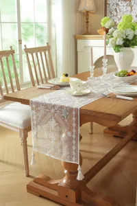 Detailed view of white lace table runner with floral embroidery and elegant tassel trim.