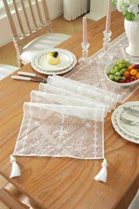 Elegant white lace table runner with floral embroidery and tassels for wedding decor.