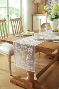 White lace embroidered table runner with delicate floral pattern and elegant tassels.