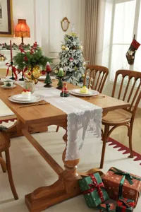Elegante camino de mesa de encaje blanco con delicados copos de nieve y campanas, ideal para Navidad.