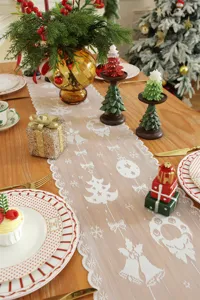 Camino de mesa navideño de encaje blanco con delicados motivos de copos y campanas.