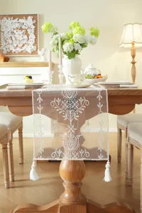 Elegant white lace table runner featuring delicate floral embroidery and charming tassel accents.